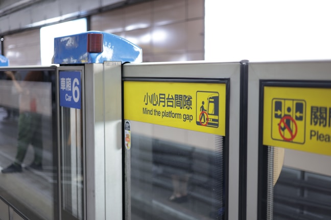 Glass safety doors at a train platform with prominent yellow warning signs indicating to mind the platform gap. The signs have both text and pictograms, and another sign designates the area as Car 6.