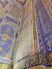 Intricately decorated wall featuring elaborate geometric and floral patterns in blue and gold. Arabic script runs along the borders and surfaces, adding a rich cultural and artistic layer to the overall design.