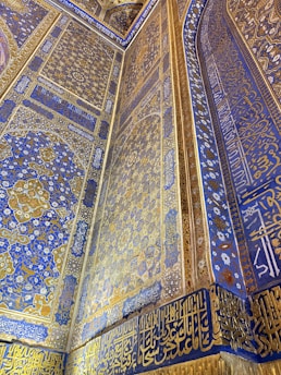 Intricately decorated wall featuring elaborate geometric and floral patterns in blue and gold. Arabic script runs along the borders and surfaces, adding a rich cultural and artistic layer to the overall design.