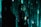 A person stands in profile against a backdrop of cascading green digital code, reminiscent of a futuristic or cyberpunk aesthetic. The person is wearing dark clothing with visible logos and has long hair. Shadows and green light interplay across their face and body, creating a mysterious atmosphere.