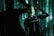 A person stands against a backdrop of projected green and black digital patterns, creating a futuristic atmosphere. The clothing features text such as 'RECESSION' and various logos. Shadows enhance the dramatic and immersive effect.