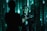 A person stands against a backdrop of green digital code patterns, reminiscent of a futuristic or virtual reality environment. The lighting creates dramatic shadows and highlights on the person's face and clothing.