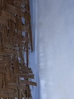 A woven structure made of interlaced, brown natural fibers, possibly bamboo or rattan, is visible next to a smooth, light-colored background wall.