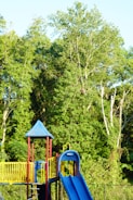A colorful playground slide surrounded by green grass and trees.