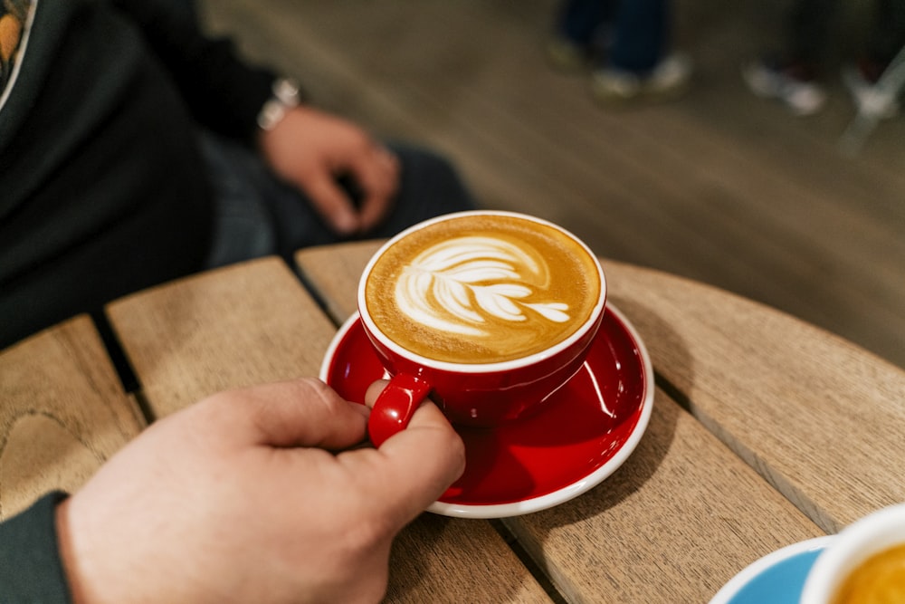 uma pessoa segurando uma xícara de café em cima de uma mesa de madeira