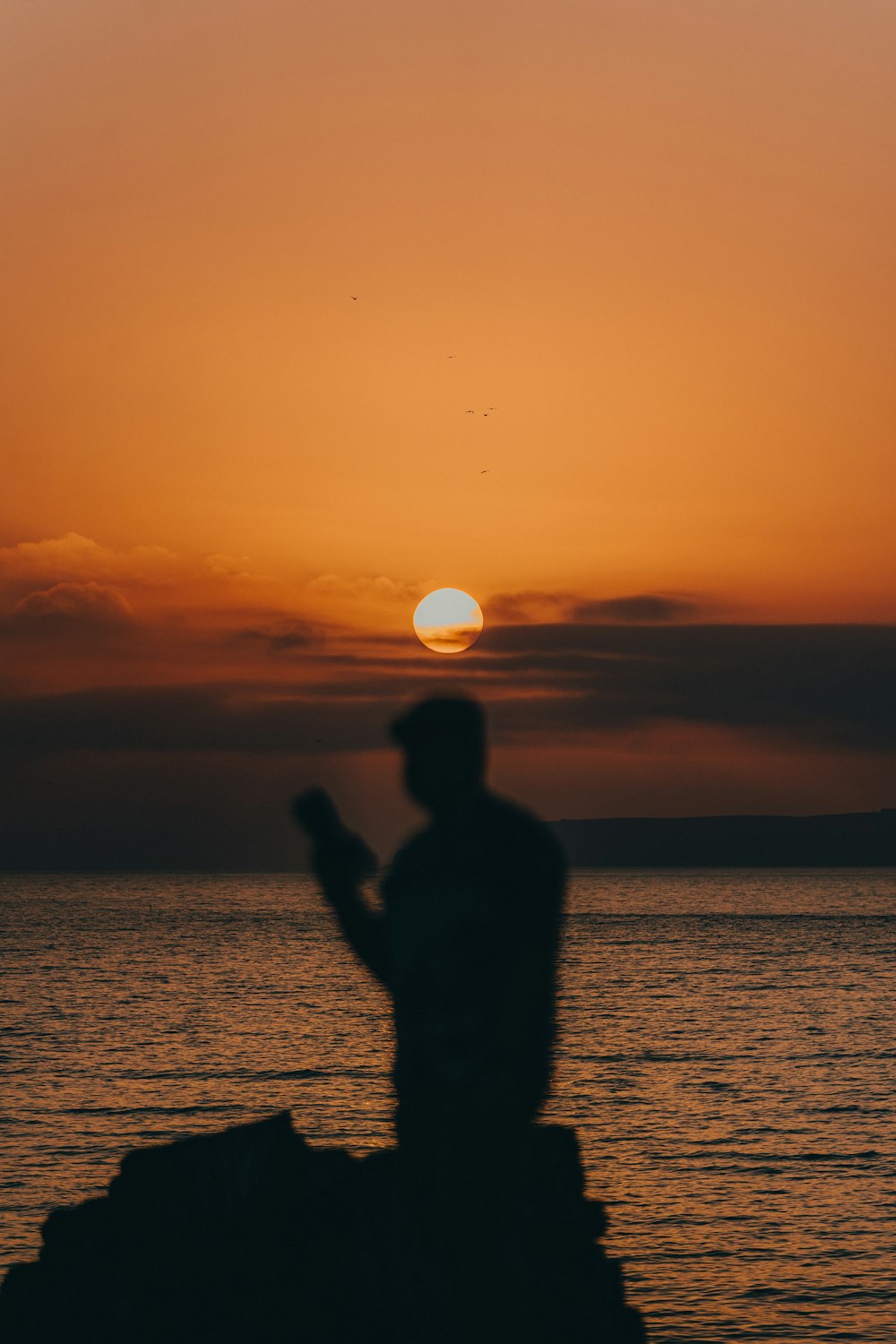 a man standing on a rock next to the ocean at sunset