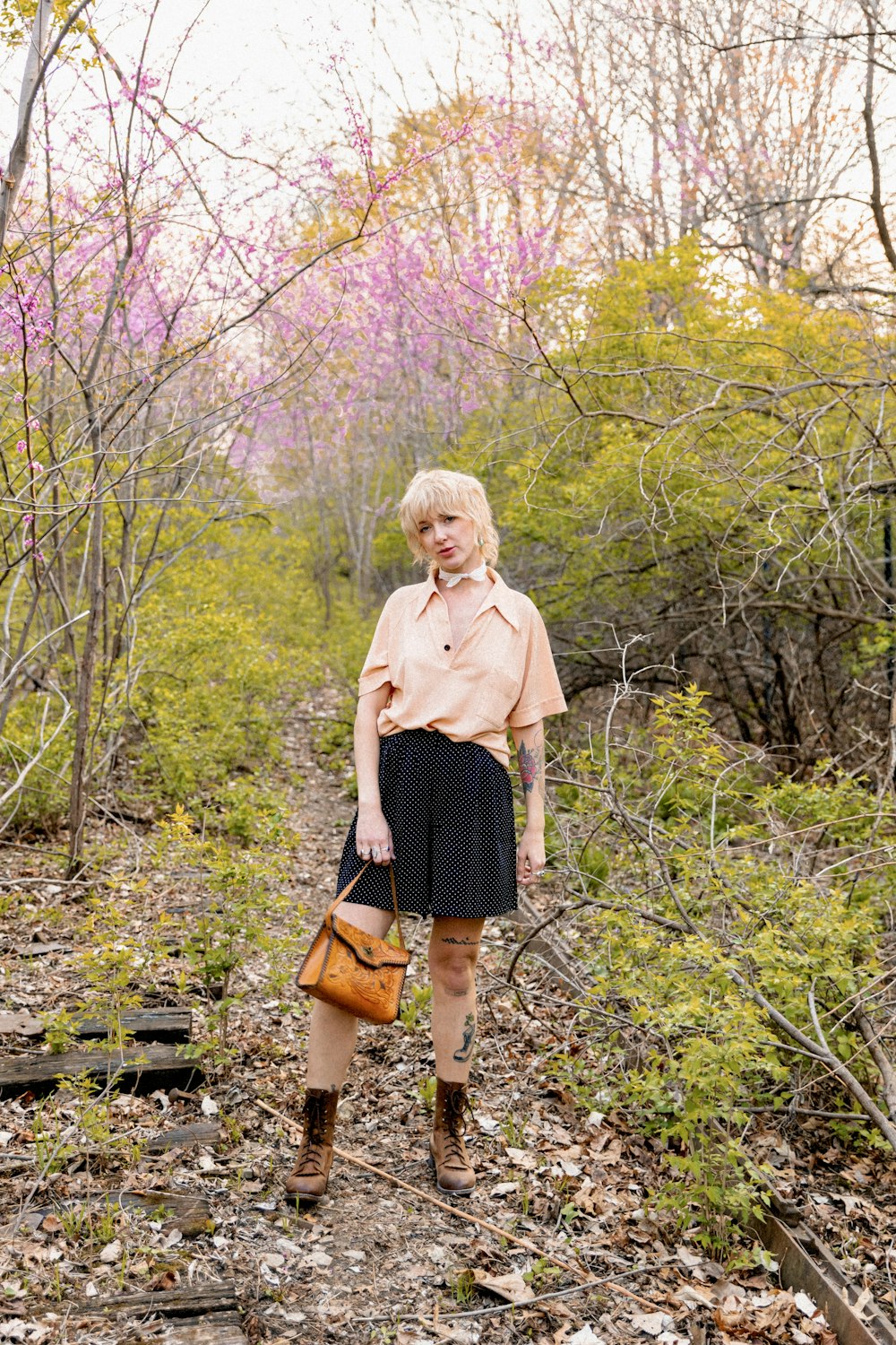 a woman standing in the woods with a handbag