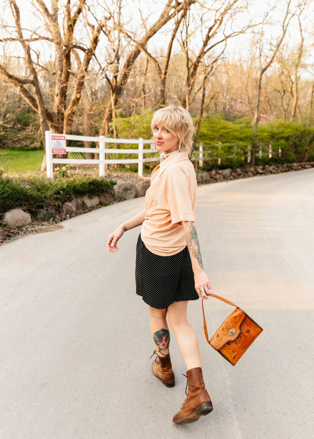 a woman walking down a road carrying a brown purse