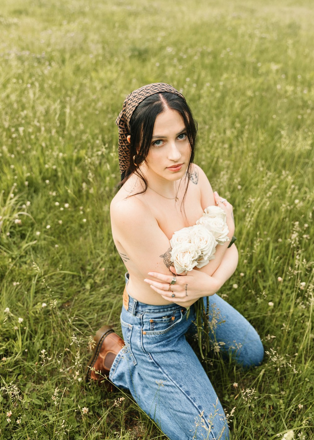 a shirtless woman sitting in a field holding a flower