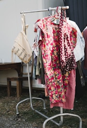 A bright, flowy dress with floral patterns hanging on a rustic wooden rack outdoors.