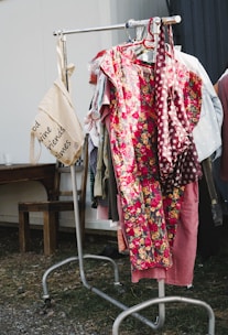 A bright, flowy dress with floral patterns hanging on a rustic wooden rack outdoors.