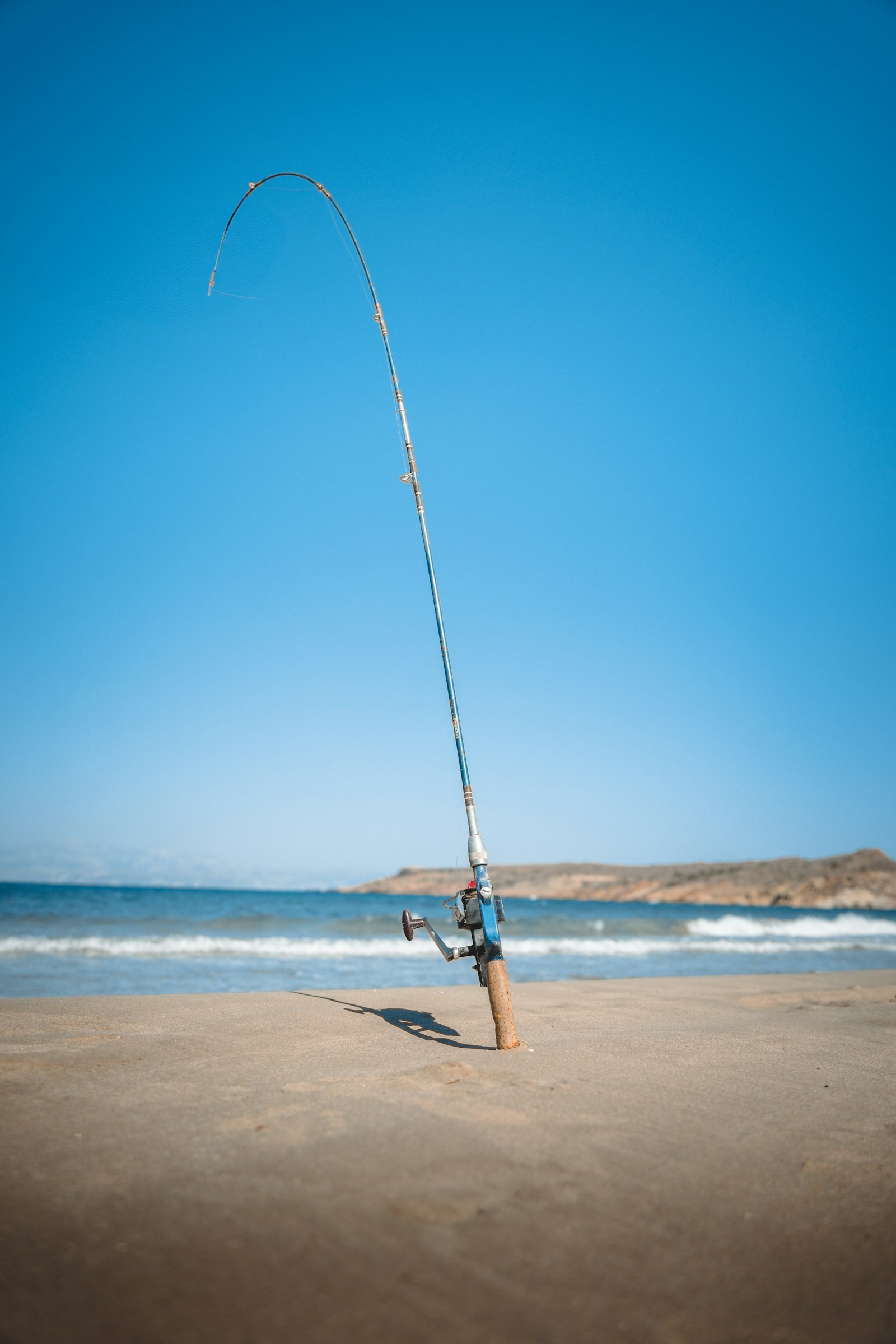 Surf fishing rod propped on sandy beach with the ocean in the background