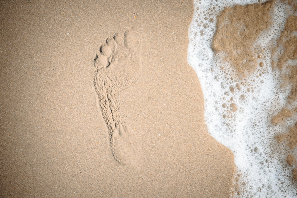 a beach with a wave coming in and a person's footprints in the sand