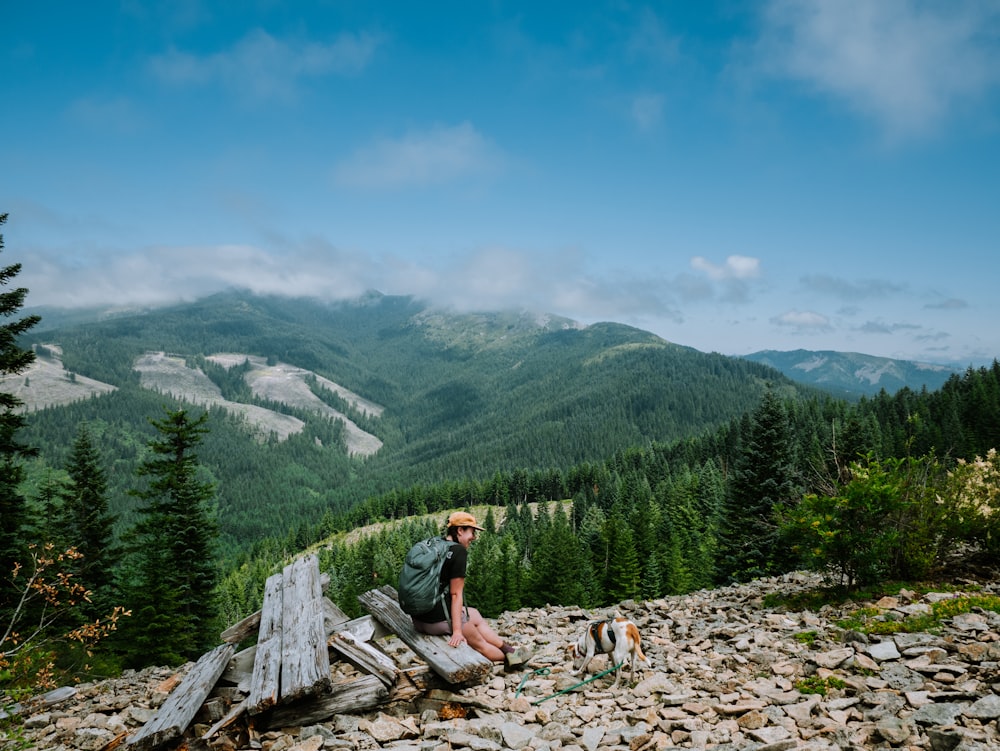 a man sitting on top of a wooden bench on top of a mountain