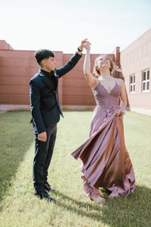 a man and woman in formal wear dancing in the grass