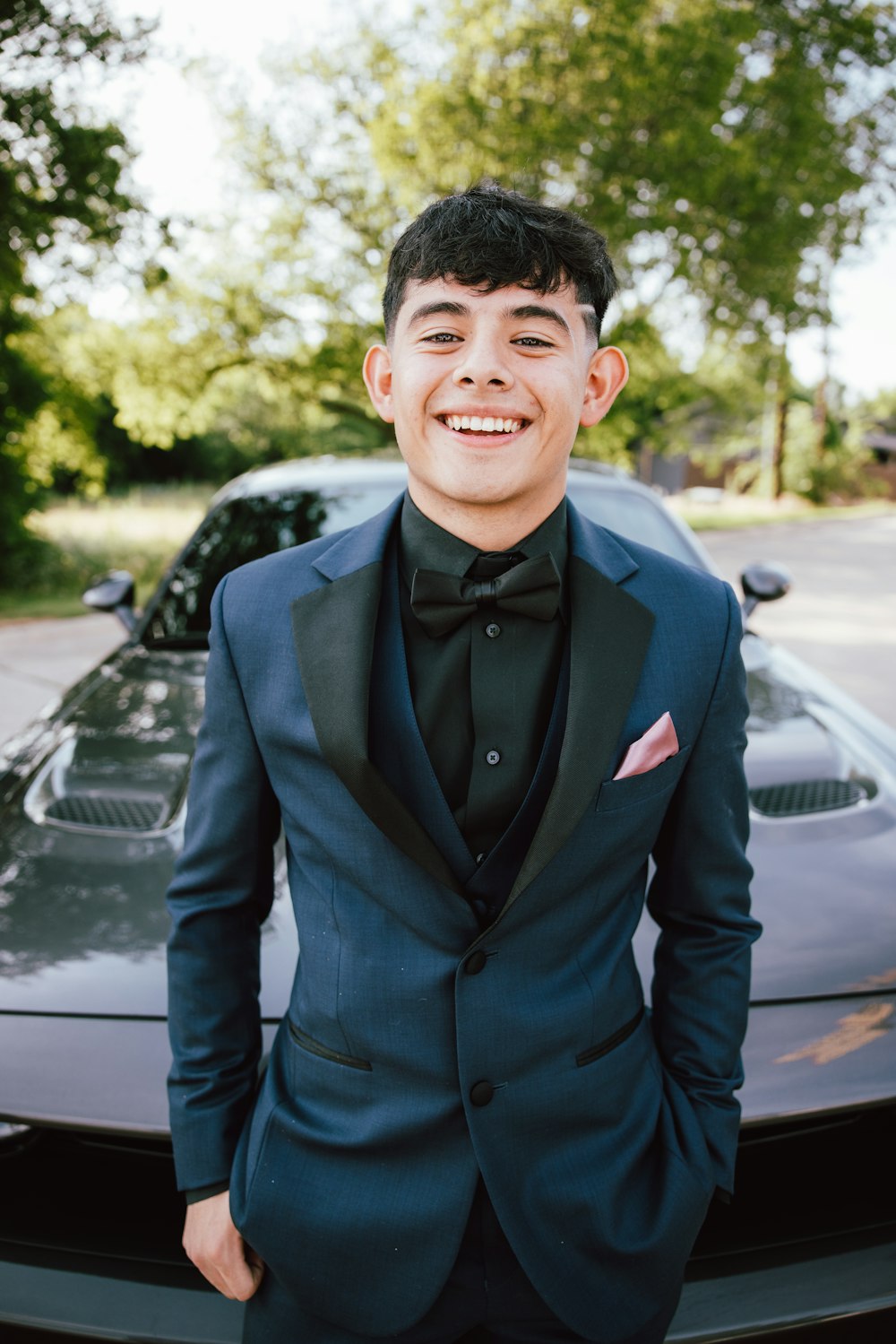 a man in a tuxedo standing in front of a car