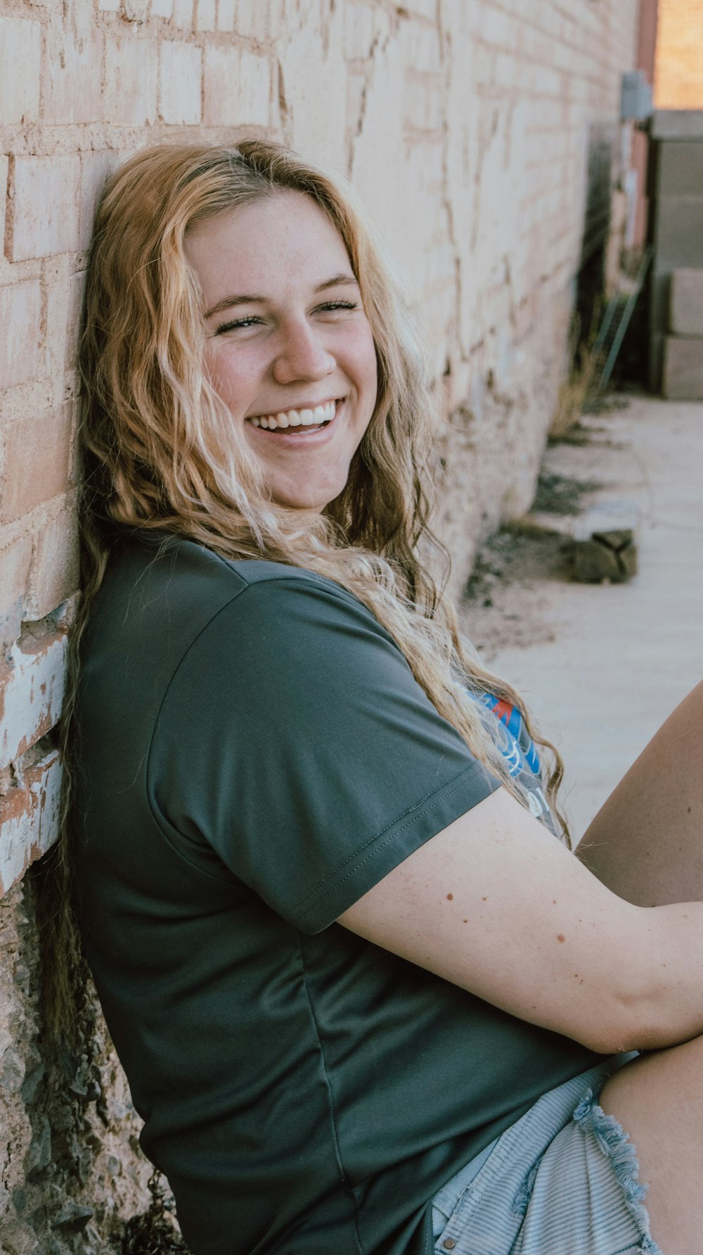 a smiling woman leaning against a brick wall