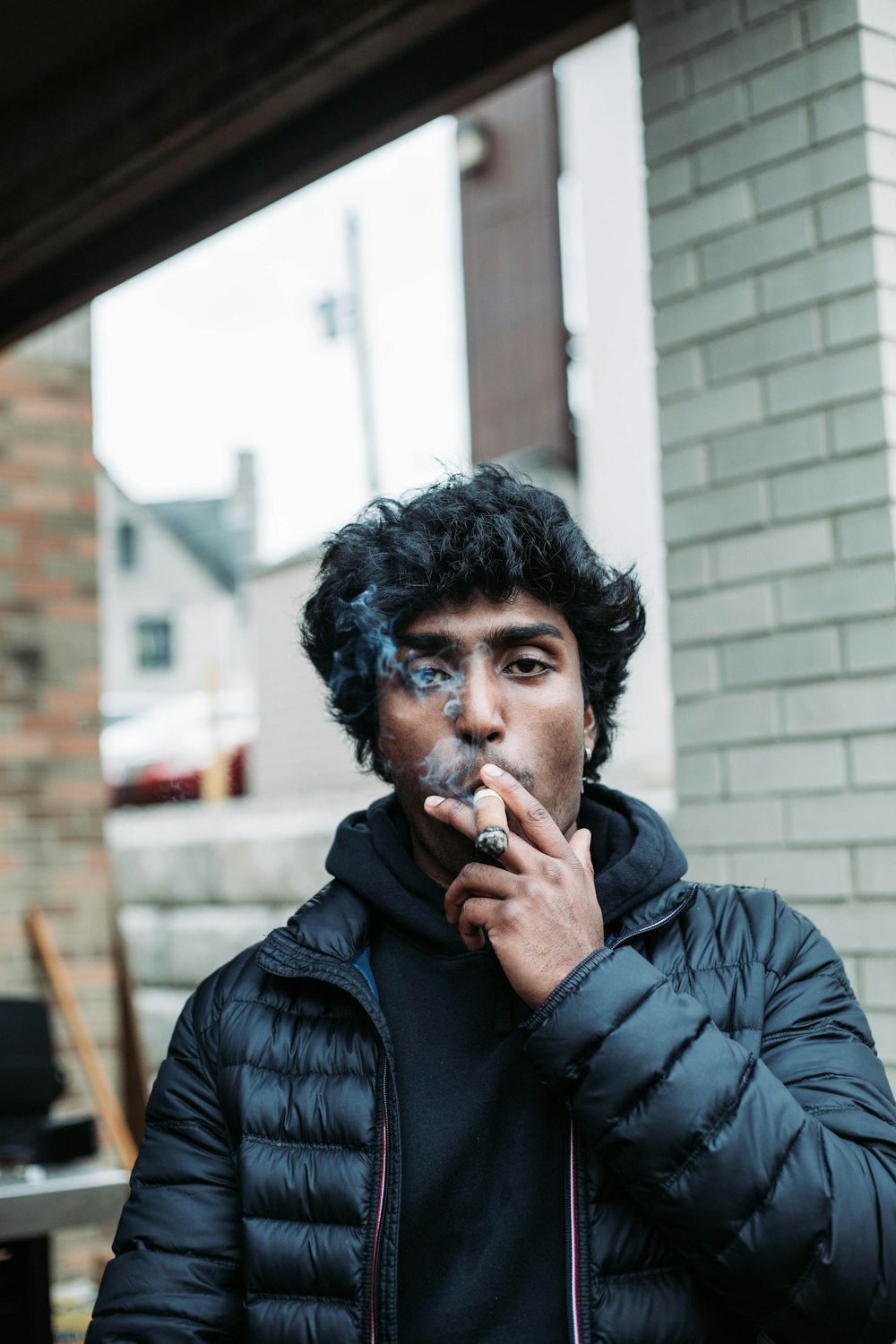 a man smoking a cigarette in front of a brick building