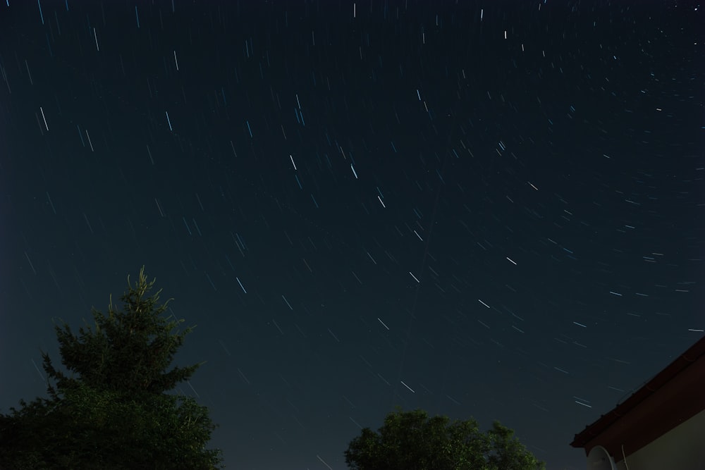 a night sky with stars above a house and trees