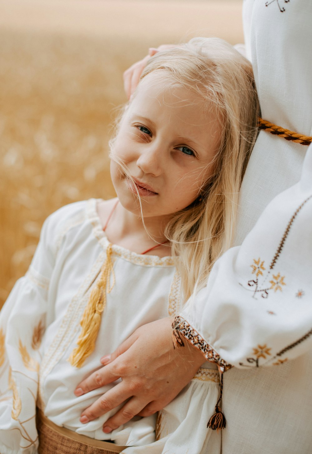 a little girl in a white dress is holding her mother's arm