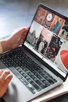 A person is operating a laptop, with the screen displaying a grid of photography images and graphics. The user interface appears to be for browsing or editing digital images. The laptop is placed on a wooden surface.