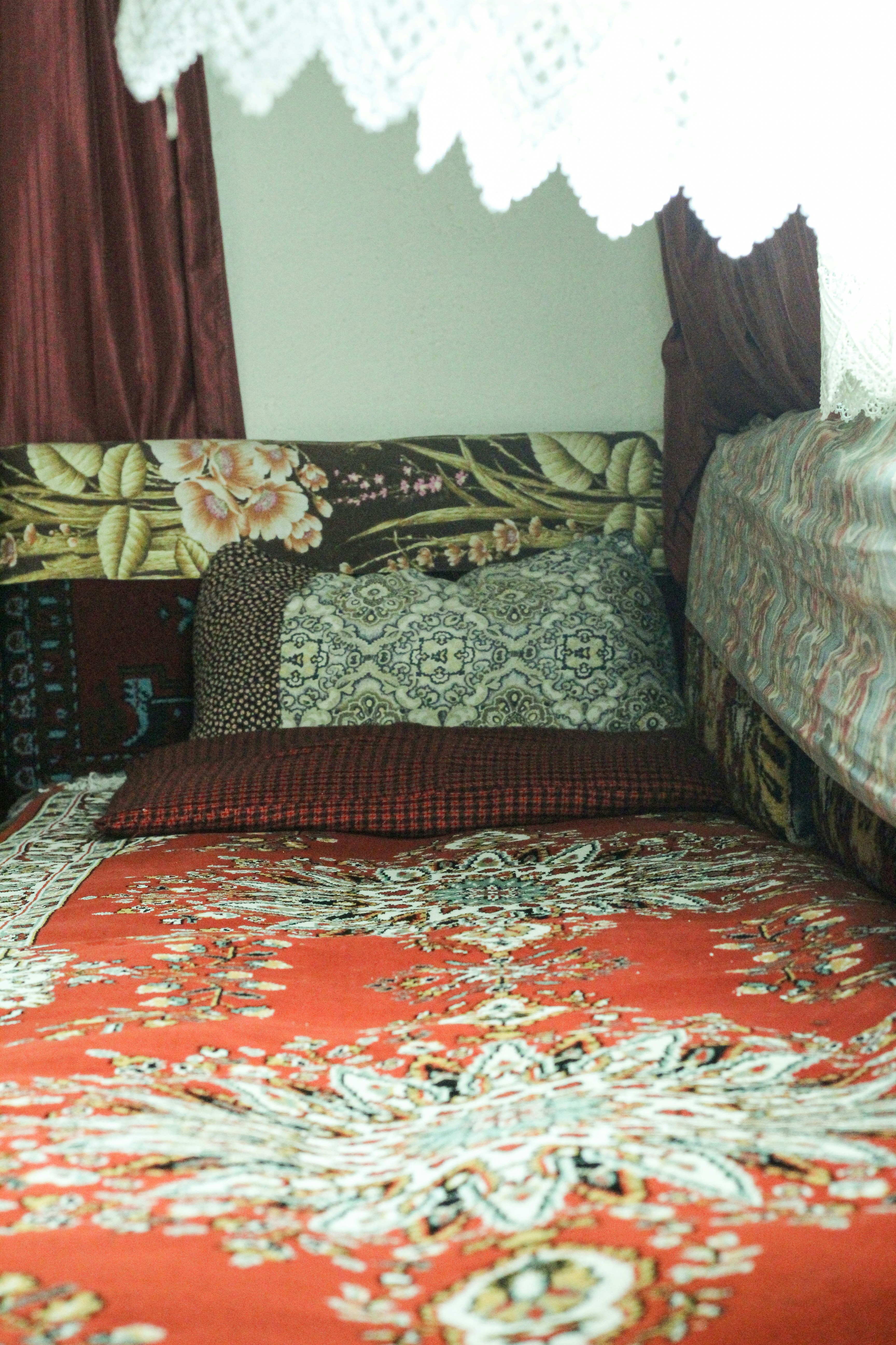 a bed with a red bedspread and a white crochet doily