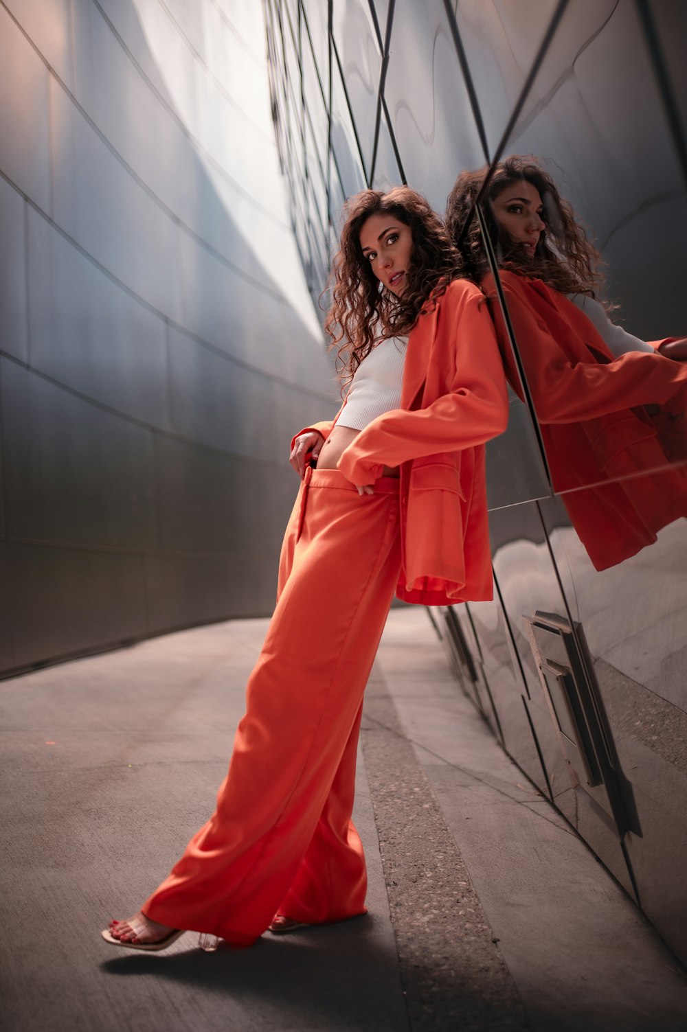 a woman in an orange outfit leaning against a wall