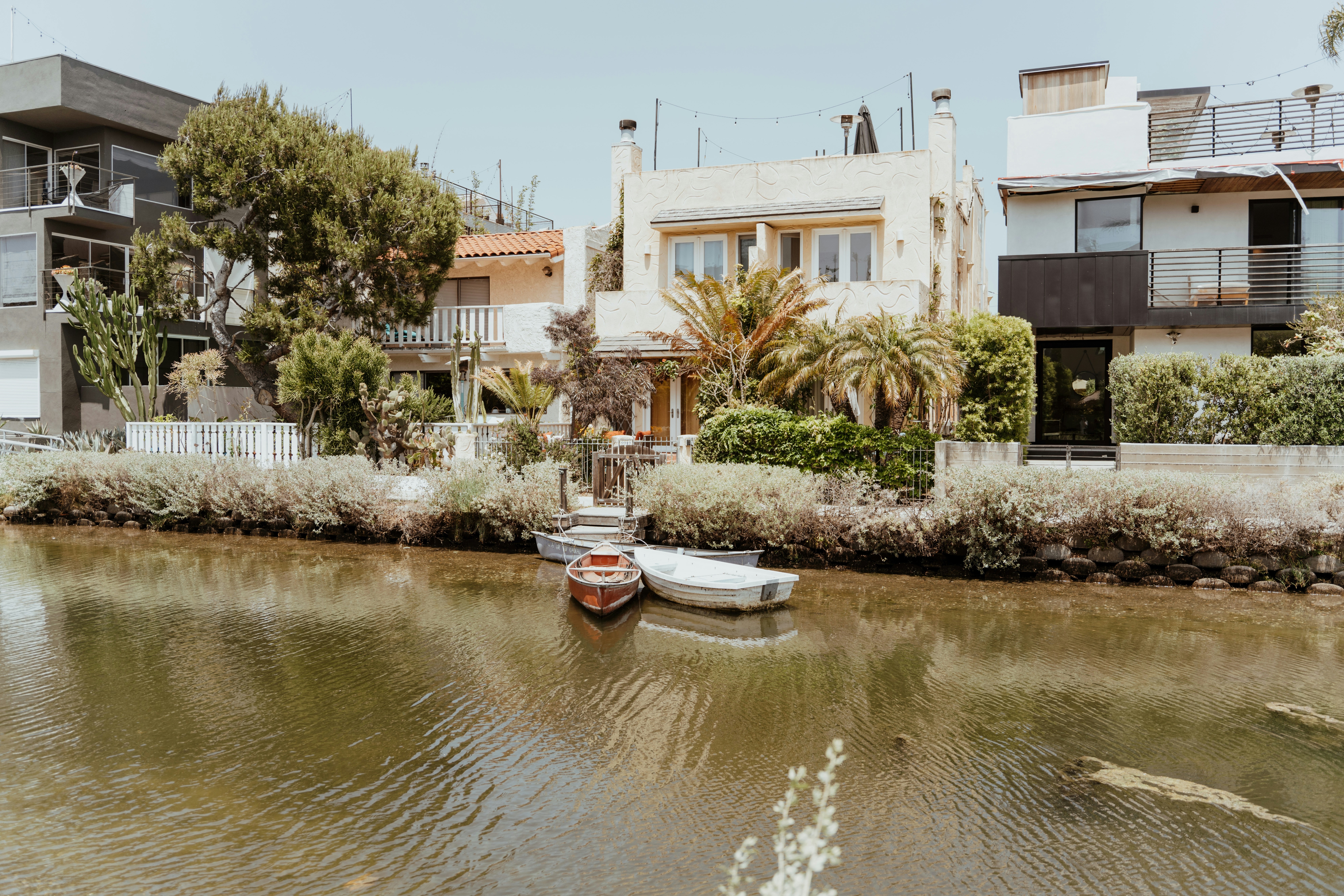 a couple of small boats floating on top of a river, Canoes along the Venice Canals in Los Angeles, California.