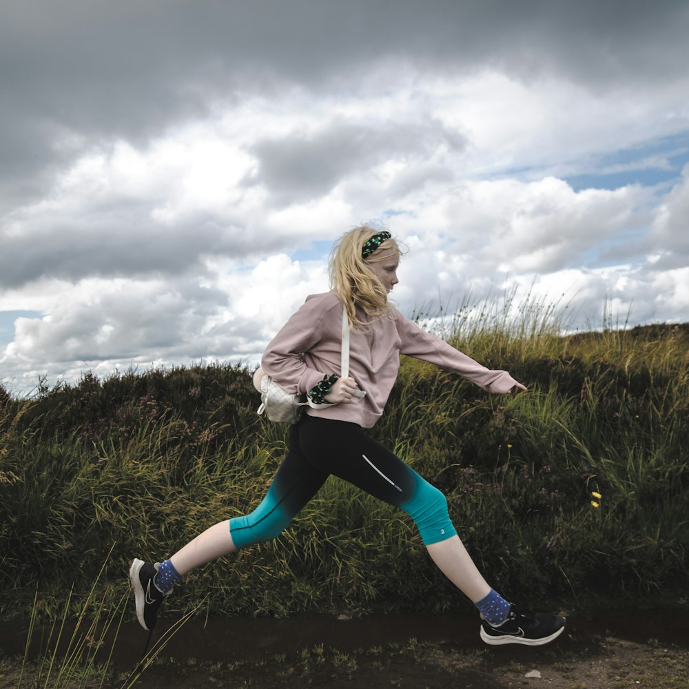 a woman running in a field with a cloudy sky in the background