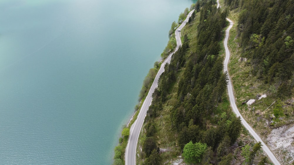 an aerial view of a winding road next to a body of water