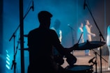 Silhouette of a drummer performing energetically on stage with blue lighting.