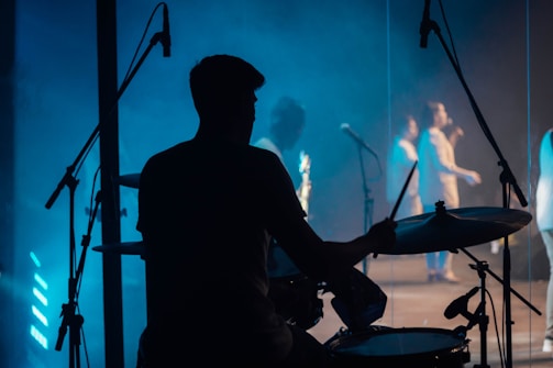 Silhouette of a drummer performing energetically on stage with blue lighting.
