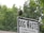 A bird stands perched atop a metal sign with the words 'DOG WASTE' prominently displayed. The sign is white with black text, and the background consists of lush green trees, indicating a natural outdoor setting.