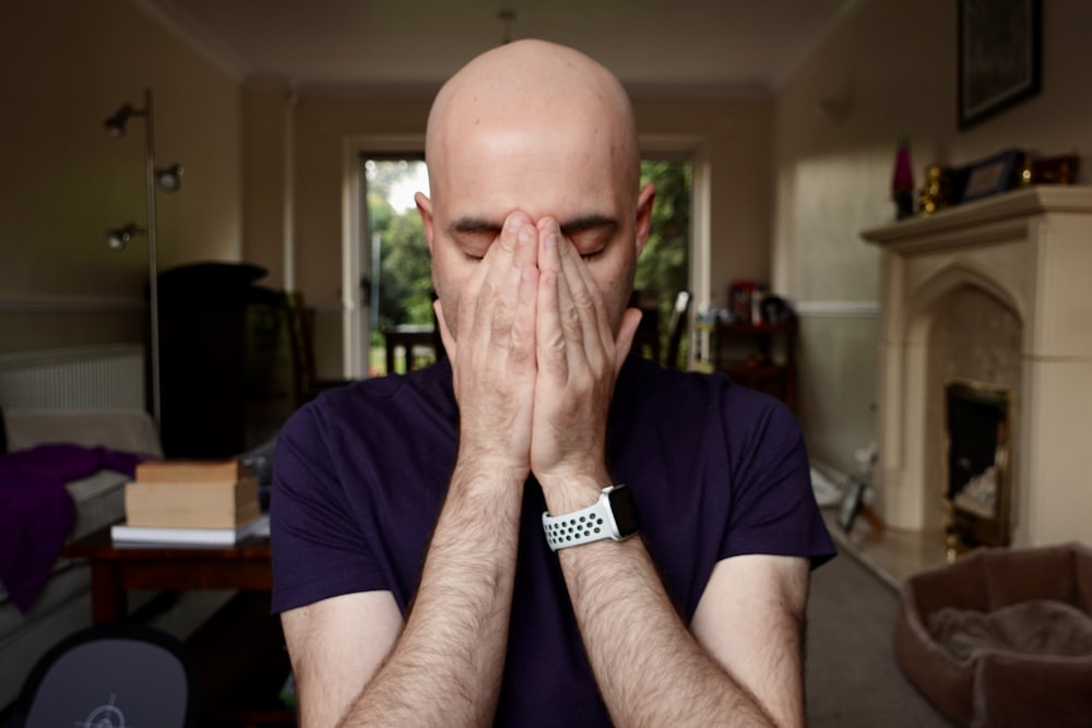 a bald man covering his face with his hands