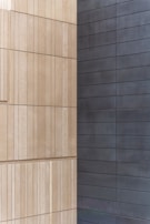 Two walls joined at a corner, with one side featuring light beige, textured rectangular panels arranged in a vertical pattern, and the other side displaying smooth, dark gray horizontal panels.