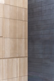 Two walls joined at a corner, with one side featuring light beige, textured rectangular panels arranged in a vertical pattern, and the other side displaying smooth, dark gray horizontal panels.