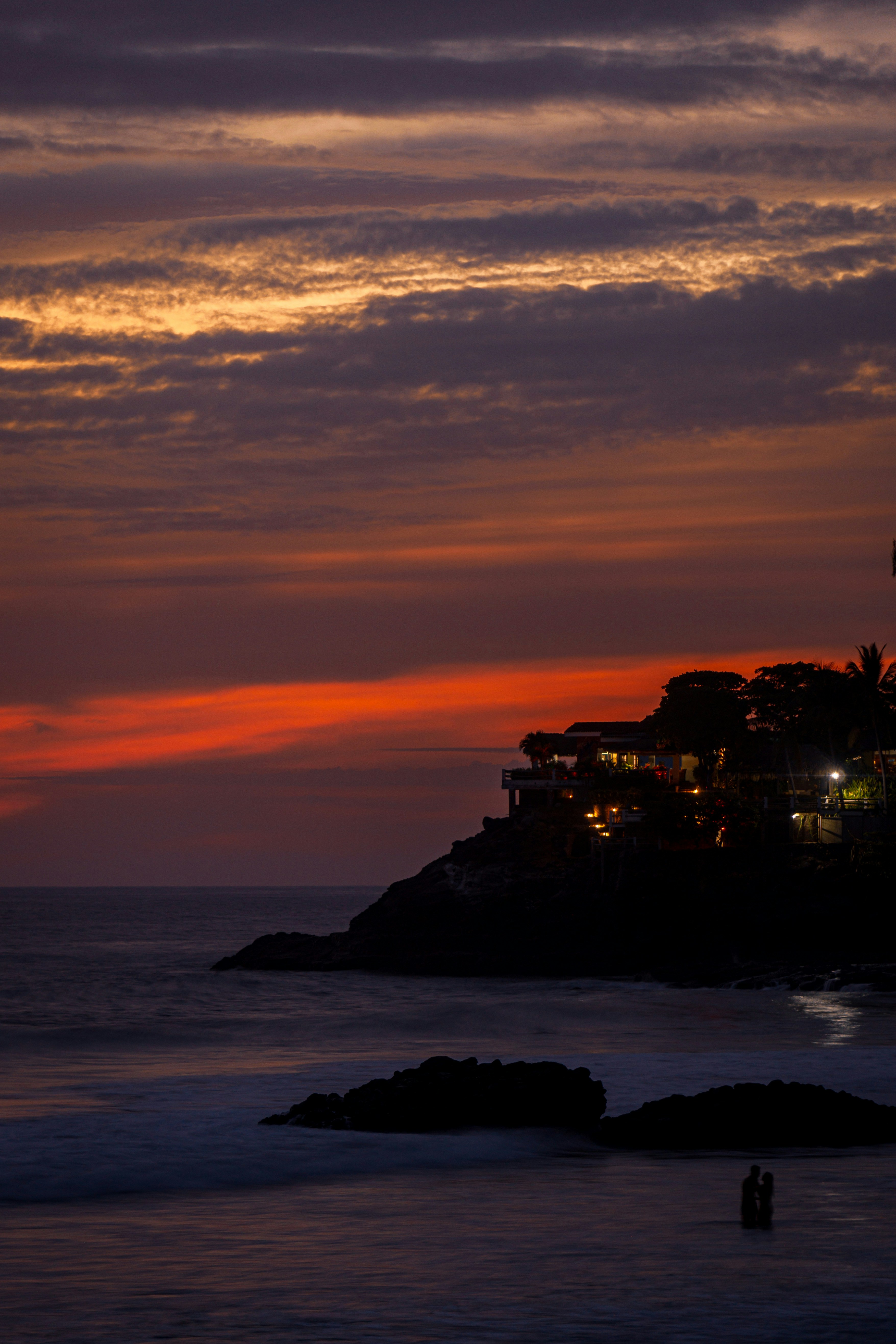 Couple silhouetted against sunset cliff, moody dark sky, dramatic golden rim light, romantic cinematic framing