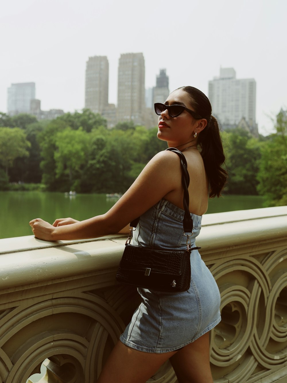 a woman in a denim dress leaning on a fence