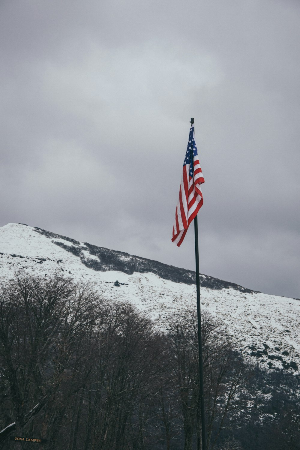 an american flag on a pole in front of a snowy mountain