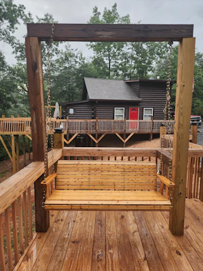 A rustic wooden swing hanging from a large tree with a view of the cabins.