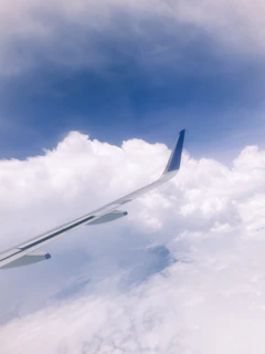 A sleek airplane soaring above fluffy white clouds under a bright blue sky, symbolizing the start of an unforgettable journey.