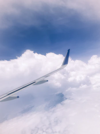 A sleek airplane soaring above fluffy white clouds under a bright blue sky, symbolizing the start of an unforgettable journey.