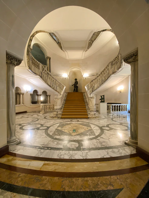 Luxurious marble staircase spiraling upwards with intricate wrought iron railings in a grand foyer