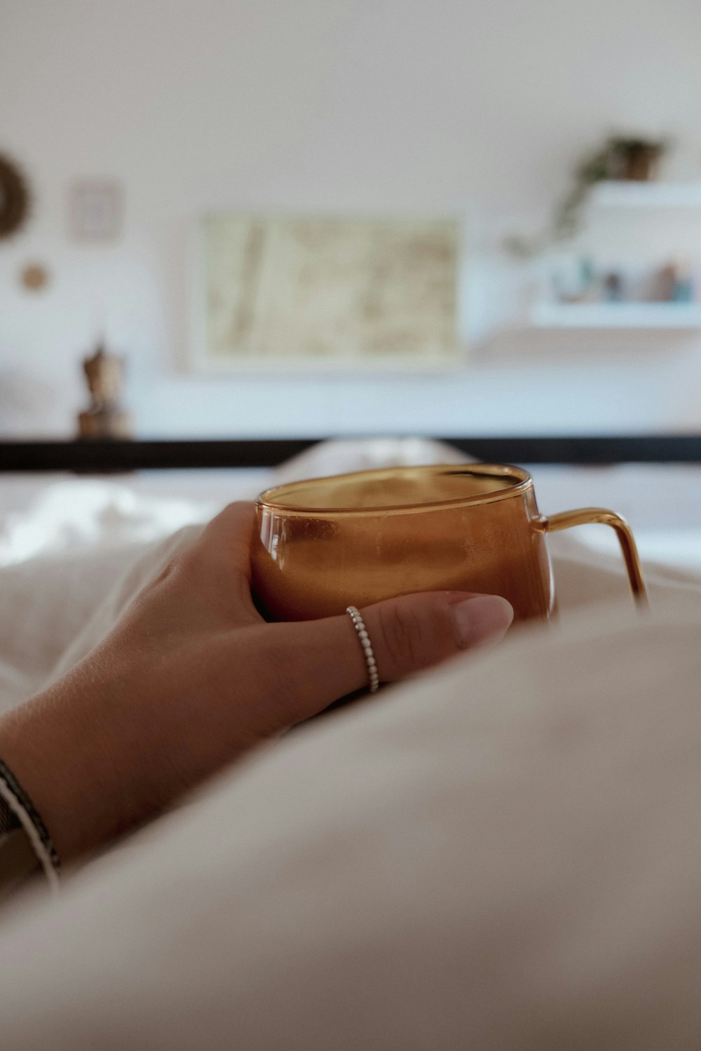 a hand holding a cup on a bed