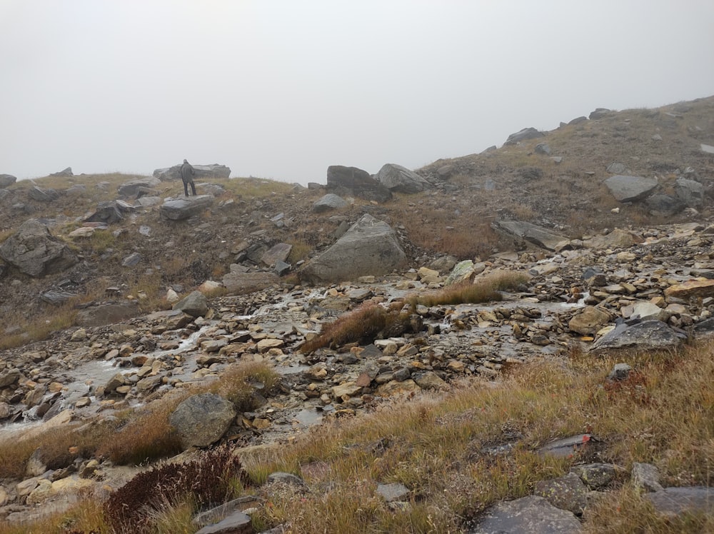 a man hiking up a rocky hill on a foggy day