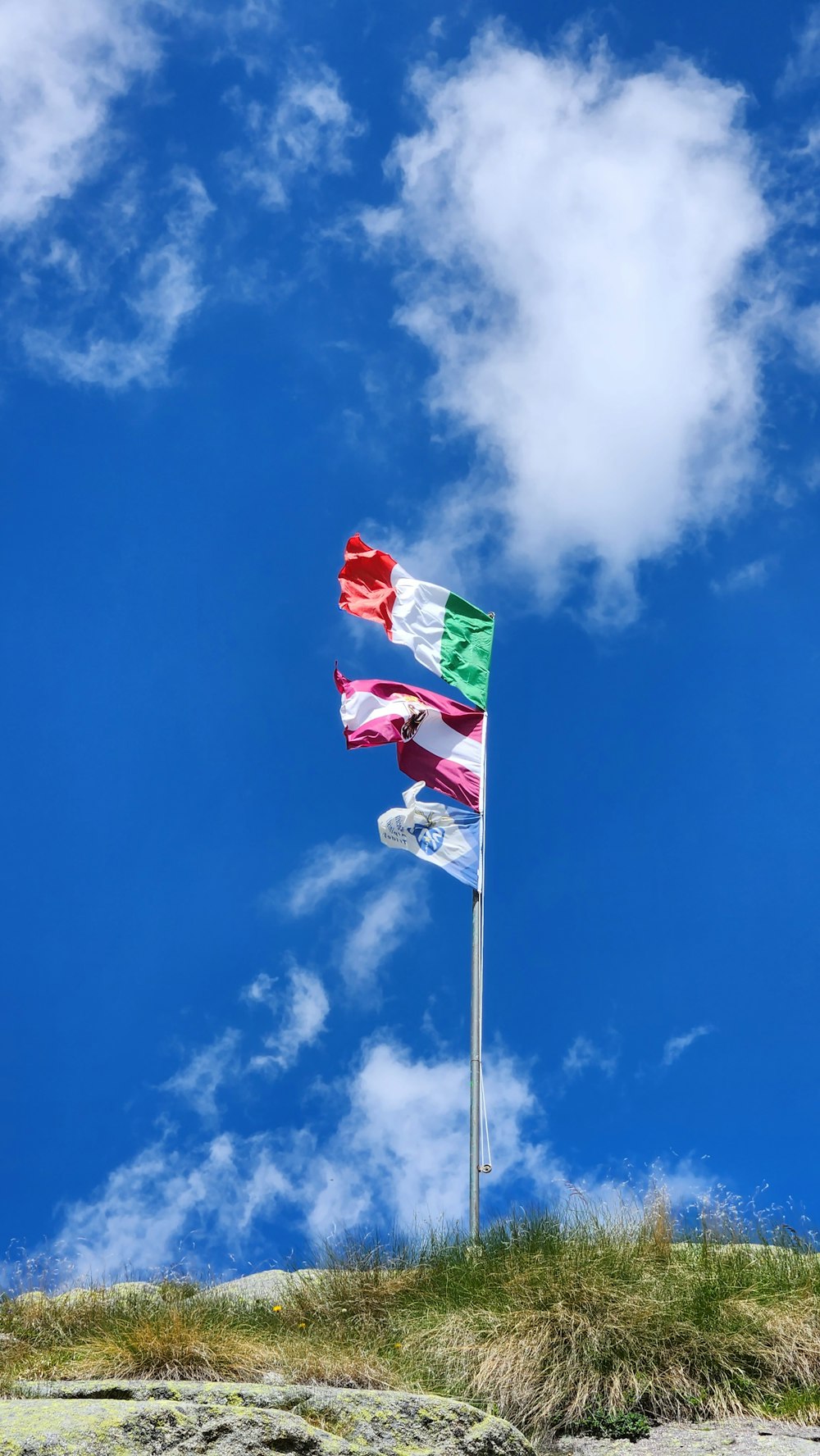 three flags are flying in the wind on a sunny day