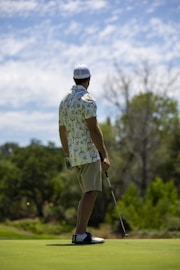 A stylish golfer wearing sleek apparel standing on a lush green Nordic golf course under a clear sky.