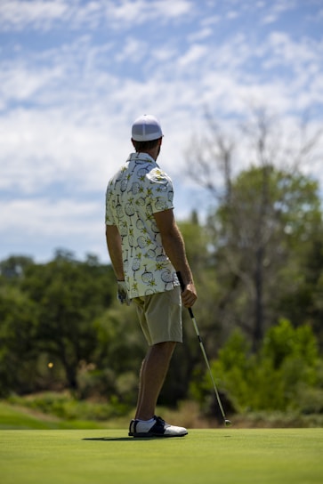 A stylish golfer wearing sleek apparel standing on a lush green Nordic golf course under a clear sky.