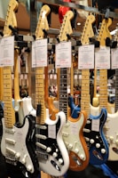 A collection of electric guitars with various colors and designs, neatly displayed in a music store. Each guitar has a label displaying its model and price.