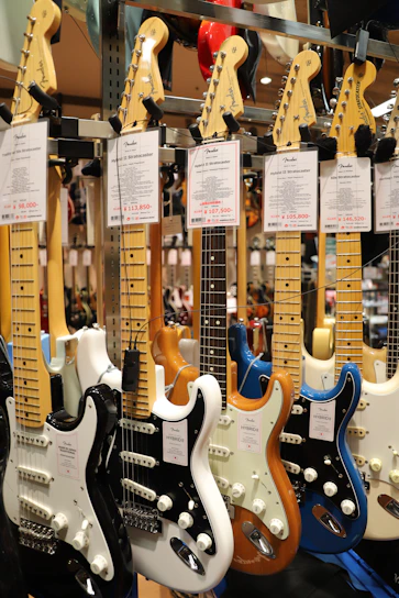 A collection of electric guitars with various colors and designs, neatly displayed in a music store. Each guitar has a label displaying its model and price.